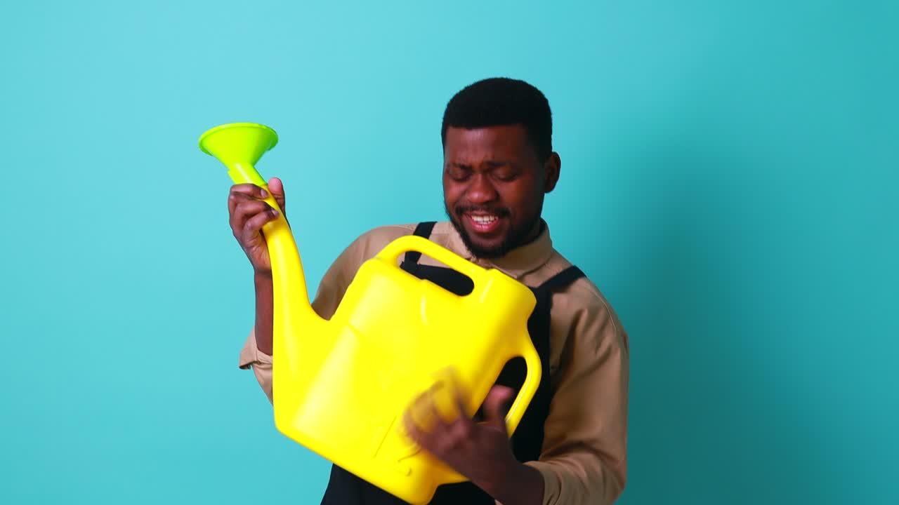 latino spain man in black apron holding yellow watering can in blue studio and playing like on guitar