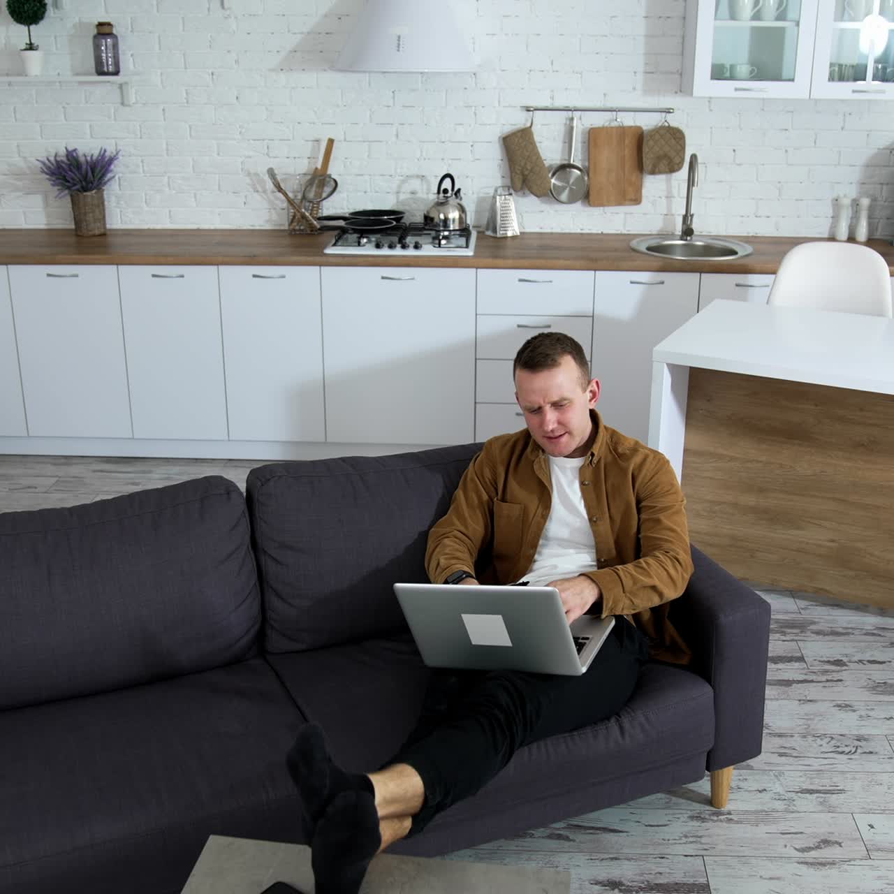 Young businessman working on a laptop. Modern kitchen background and man freelancer sitting in a couch with a laptop. Remote job