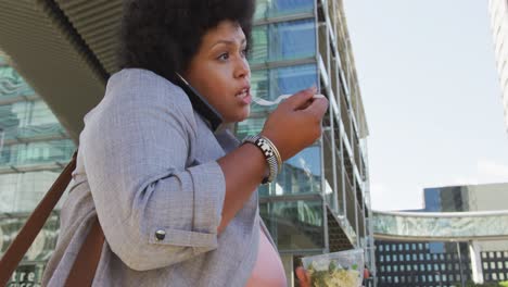 plus size biracial woman walking with smartphone and salad in city