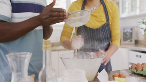 Mid-section-of-diverse-couple-wearing-apron-and-baking-in-kitchen