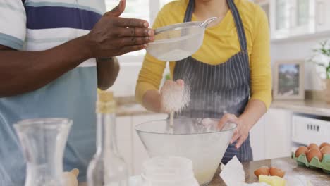 sección media de una pareja diversa con delantal y horneando en la cocina