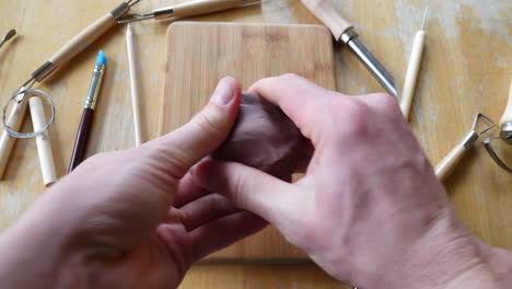 close up on the hands of an artist or sculptor making a figurine out of brown modeling clay in his art studio with tools on the table