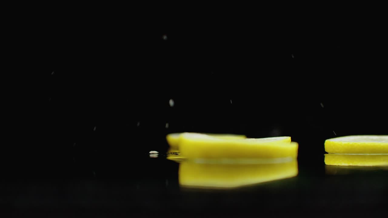 нарезанные лимонные кольца падают с брызгами воды на стакан на темном фоне. сочные цитрусовые