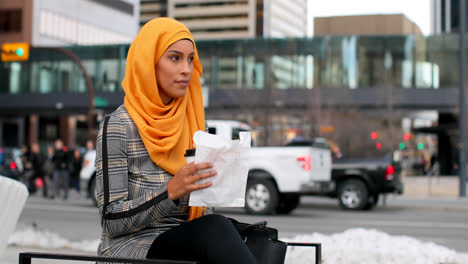 Vista-Lateral-De-Una-Joven-Asiática-Con-Hijab-Comiendo-Comida-En-La-Ciudad-4k