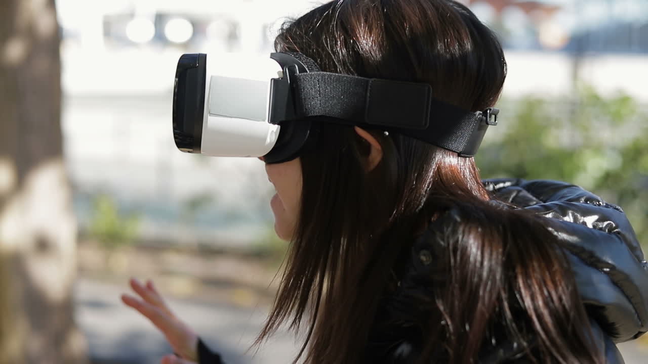 Amazed young dark-haired woman in warm black waistcoat wearing virtual reality glasses in early autumn park