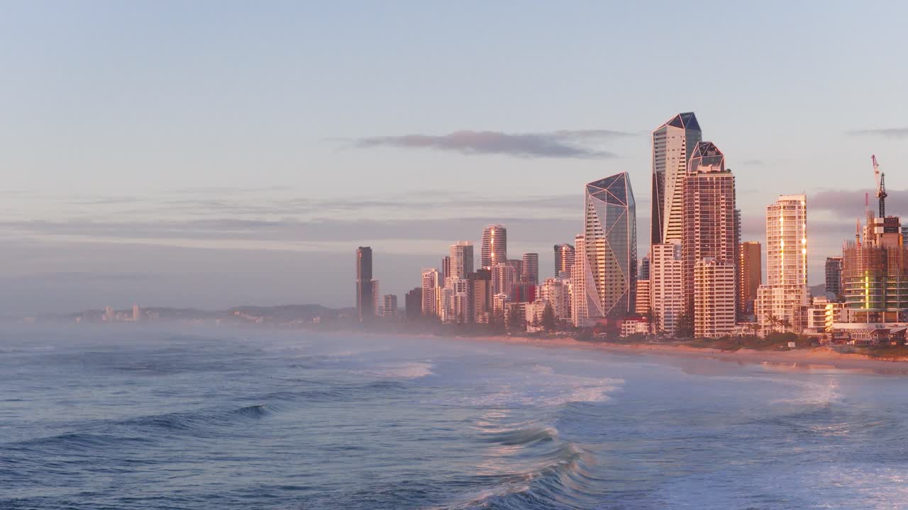 Drone footage captures Gold Coast's skyline and ocean waves at sunrise, highlighting modern architecture and serene coastal beauty