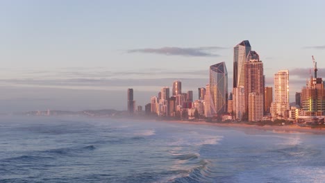 drone footage captures gold coast's skyline and ocean waves at sunrise, highlighting modern architecture and serene coastal beauty