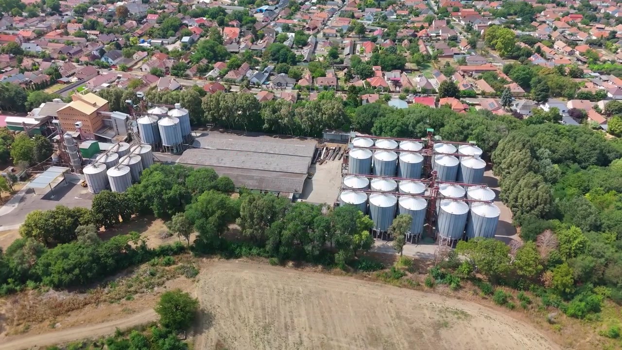 Hajdúböszörmény, Hungary animal feed store and grain silo complex beside farmland and residential areas in summer, with industrial storage and logistics infrastructure filmed by drone
