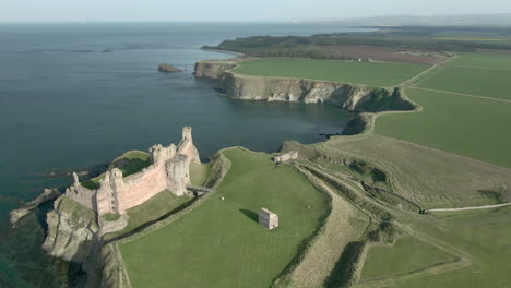 an aerial view passing over tantallon castle ruin with the castle to the left-hand side of frame on a sunny day, east lothian, scotland