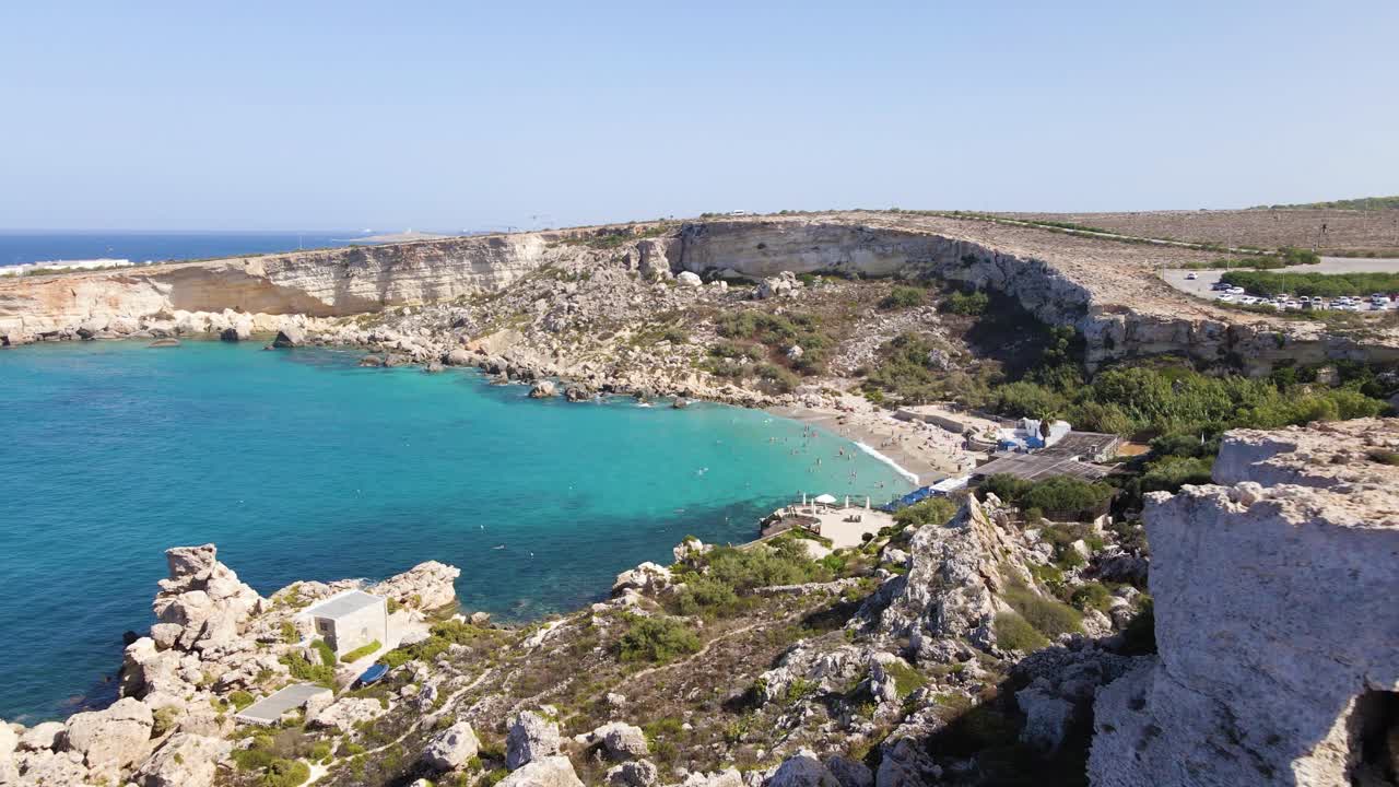 Prospettiva aerea elevata di una baia sulla spiaggia di Paradise Bay circondata da imponenti scogliere calcaree, che mostra acqua turchese, servizi sulla spiaggia e la costa mediterranea