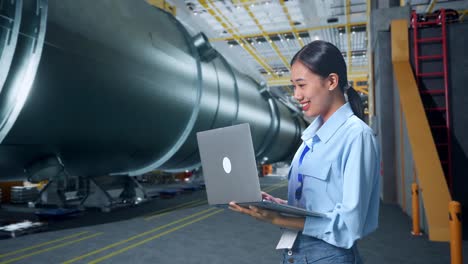 side view of asian business woman using laptop computer in pipe manufacturing factory