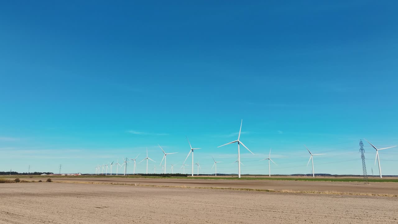 The low angle view of a large windmill farm in the fields during springtime showcases the towering turbines against a clear skies.