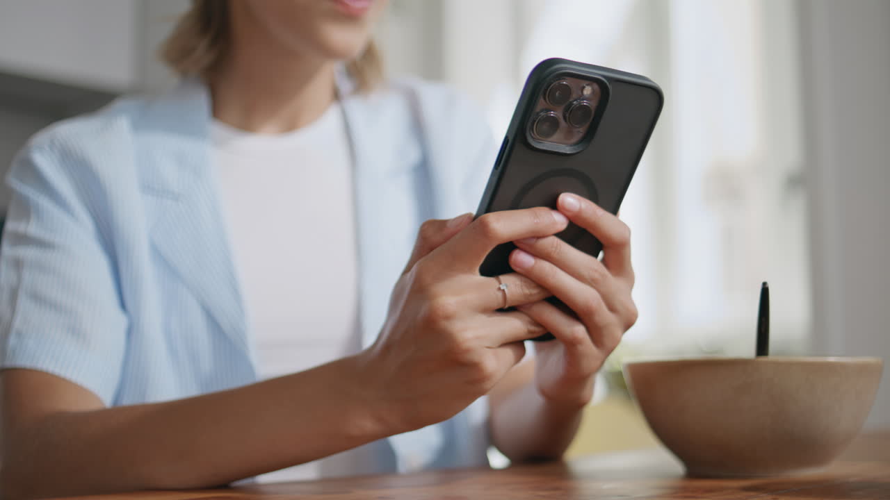 Closeup woman holding smartphone in hand in sunny kitchen. Relaxed female browse