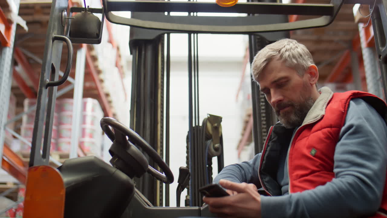 A man using a smartphone while sitting on a forklift in a warehouse