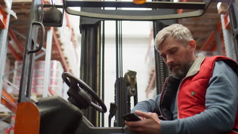 a man using a smartphone while sitting on a forklift in a warehouse
