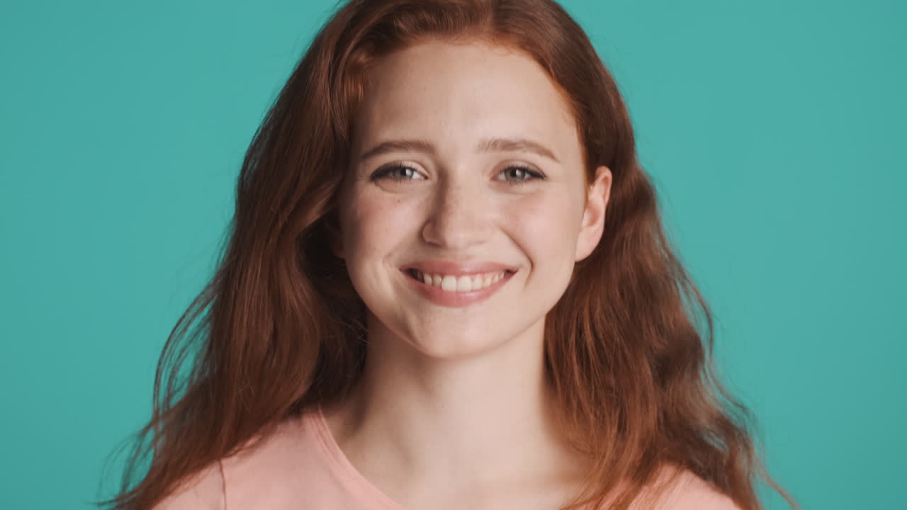 una chica pelirroja frente a la cámara sobre un fondo turquesa.