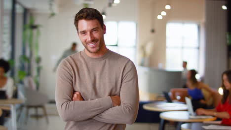 portrait of smiling businessman standing in busy modern open plan office