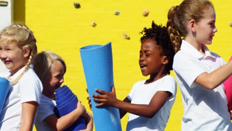 niños de la escuela sosteniendo colchonetas de yoga e interactuando entre sí