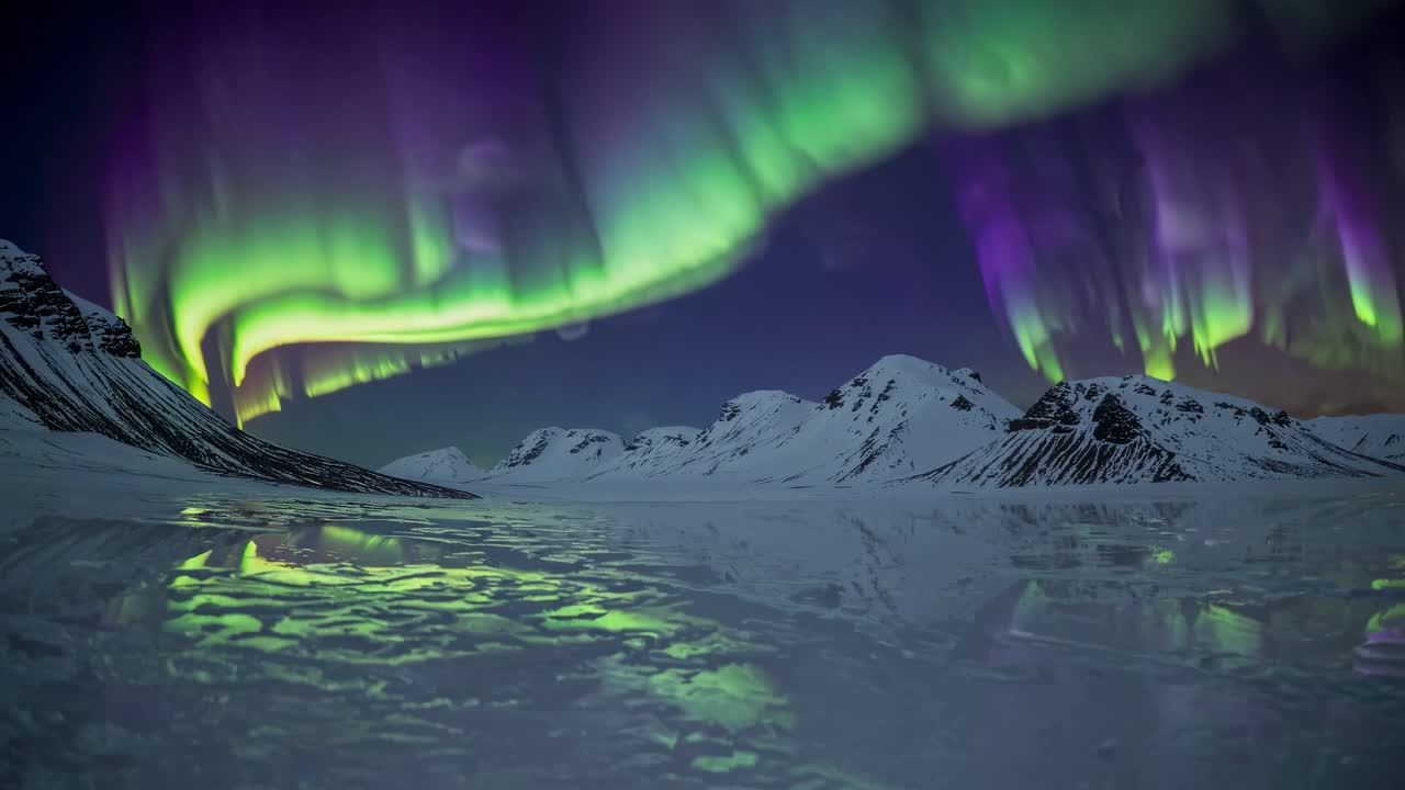 A wide-angle video captures the mesmerizing aurora borealis over snowy mountains, reflecting vibrant