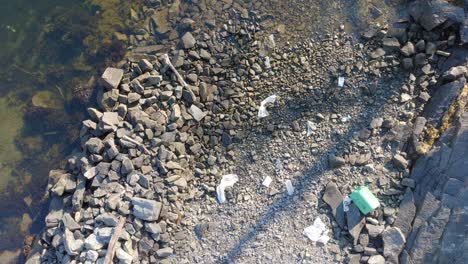 Aerial-zoom-out-above-small-rocky-beach-littered-with-plastic-waste-in-Norway