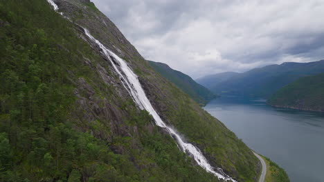 cascading white water from langefoss waterfall drips down steep alpine cliff into fjord below