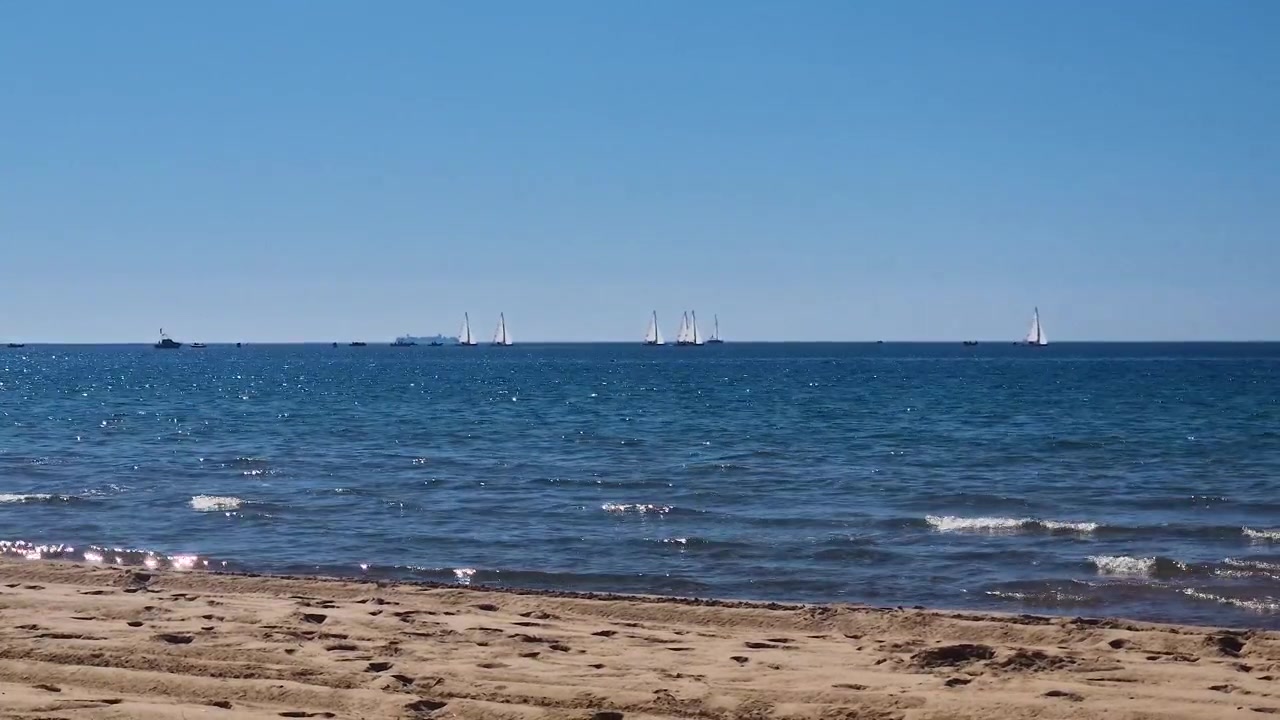 Sailboat glides on peaceful sea near Spain’s beach coastline under clear blue sky.