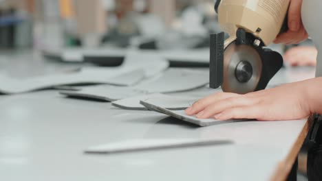 female worker on a sewing manufacture uses electric cutting fabric machine. sewing production line