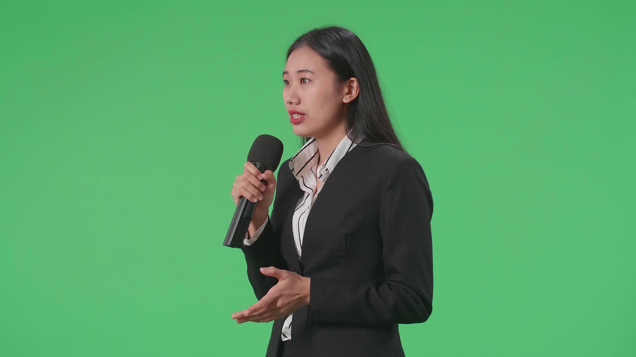Side View Of Asian Woman Journalist Speaks Into A Microphone On The Green Screen