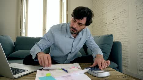 young angry and worried man working with laptop at home looking at bills and paying bills in home finance concept.