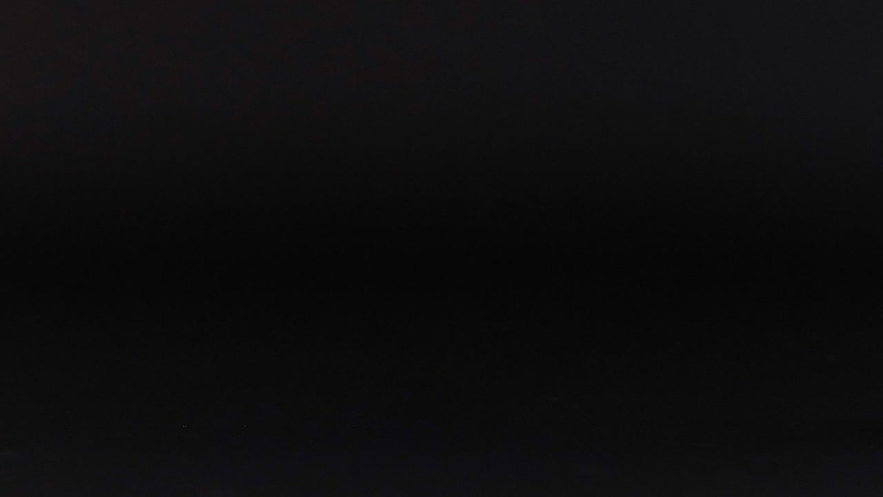 An orange tennis ball is positioned on a dark surface, highlighting its vibrant color and texture.