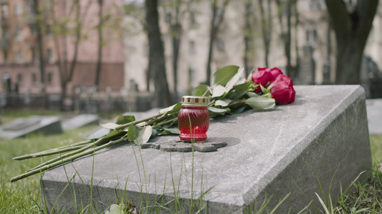 묘지에 있는 묘비에 있는 빨간 장미와 촛불을 가까이서 볼 수 있습니다.