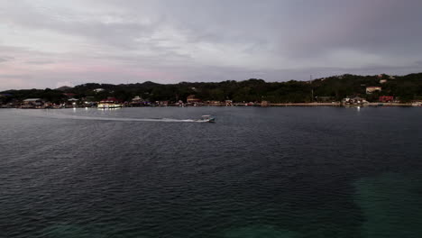 Aerial-push-in-on-a-motorized-boat-being-driven-across-the-open-waterfront-near-the-coast-of-Roatan,-Honduras