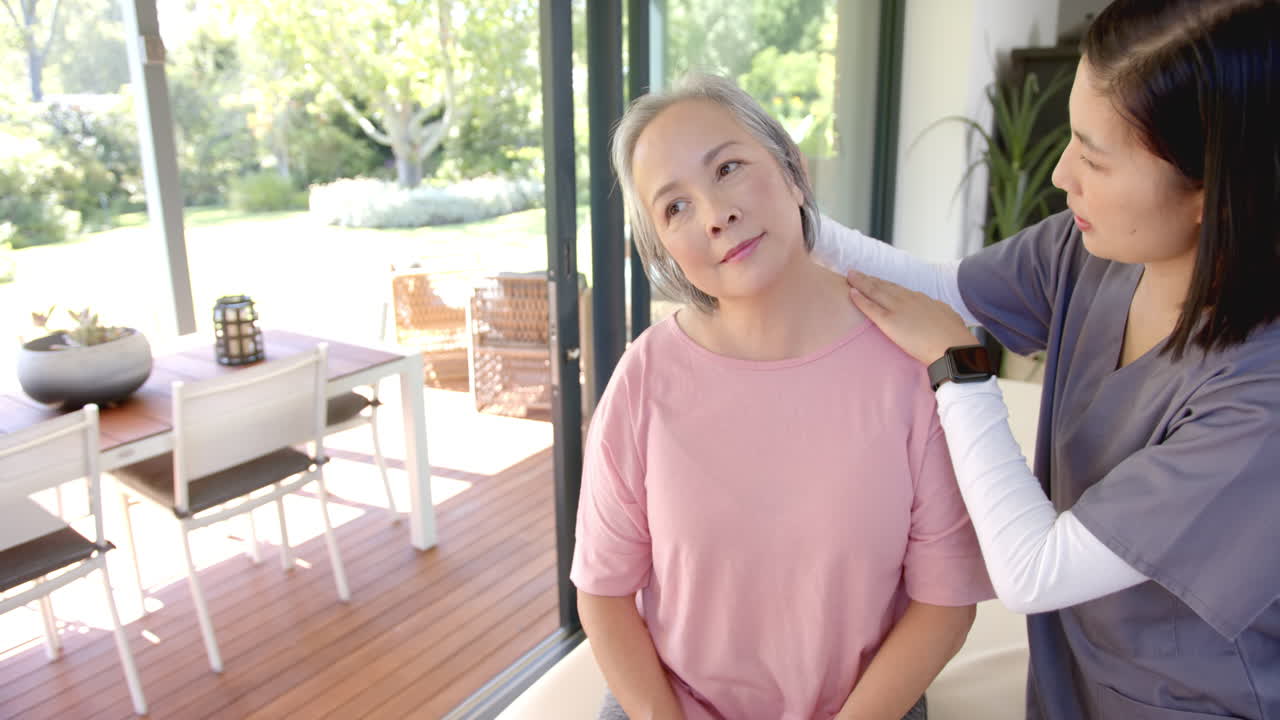 Physiotherapist giving shoulder massage to senior asian woman in home setting