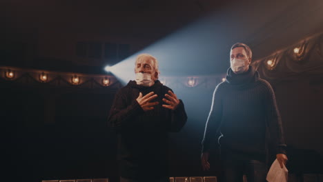 actors in masks quarreling on stage couple in medical masks arguing with each near near elderly man while rehearsing quarrel scene on stage in theater during pandemic