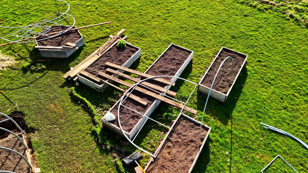 Rectangular garden beds with soil and hoop frames being assembled on green grass in a rural European setting.