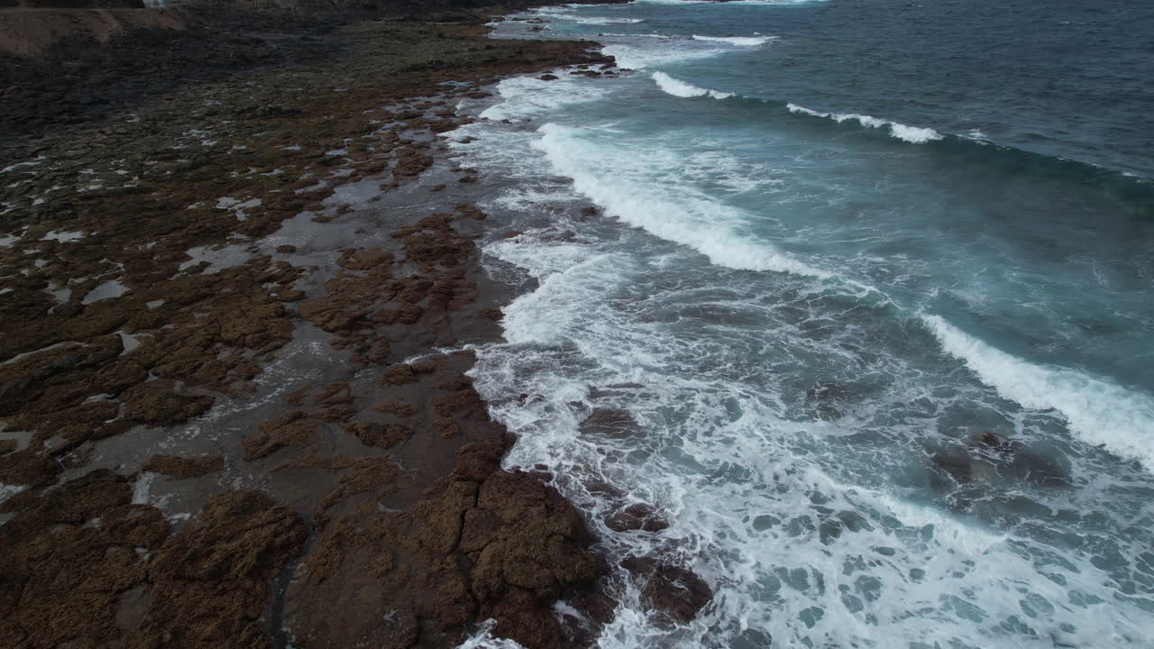cinematic aerial shot over the shore with rocks of the beach of Punta de Galdar on the island of Gran Canaria and revealing the houses near the coast