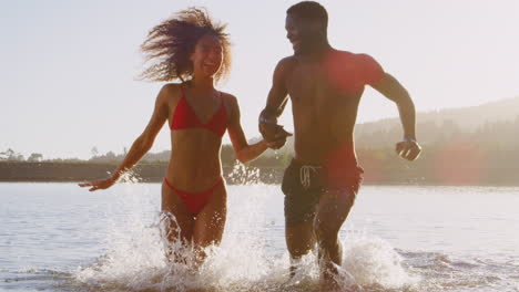 Una-Joven-Pareja-De-Raza-Mixta-Corriendo-Y-Chapoteando-En-Un-Lago.