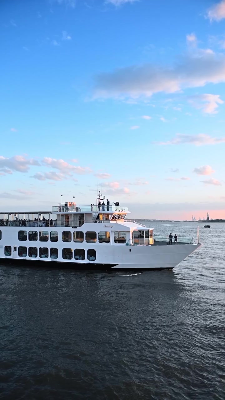 New York, USA, 25. december 2025: Passagerbåd sejler i havn ved solnedgang nær Frihedsgudinden. Hvidt fartøj flyder på vandet under blå himmel med gylden time-belysning