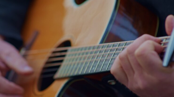 Gitarist akustik gitarda etüt çalıyor, ellerin, bileklerin, parmakların, perdelerin ve tellerin yakın çekim görüntüsü.
