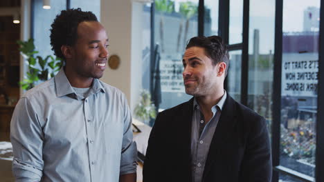 portrait of two businessmen standing in modern open plan office together