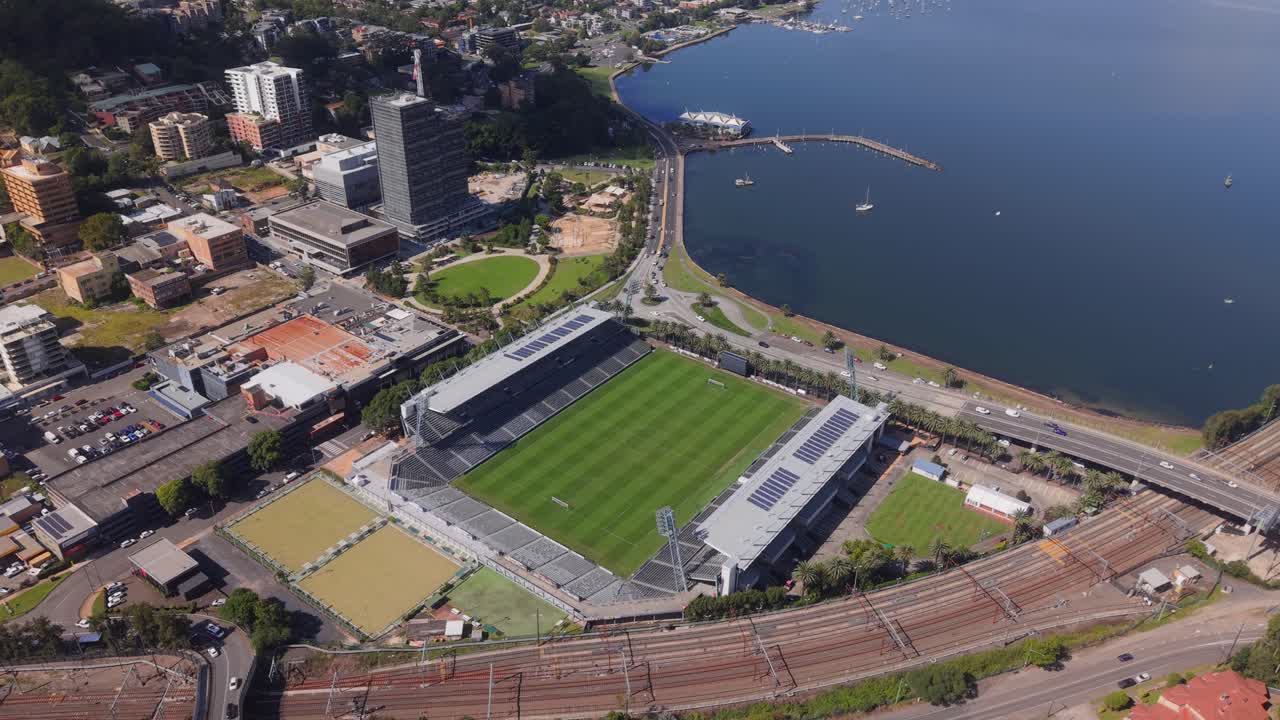 Wide aerial ascend overview of Polytech Stadium in Gosford with visible stands, field, and nearby coastline, Central Coast NSW Australia