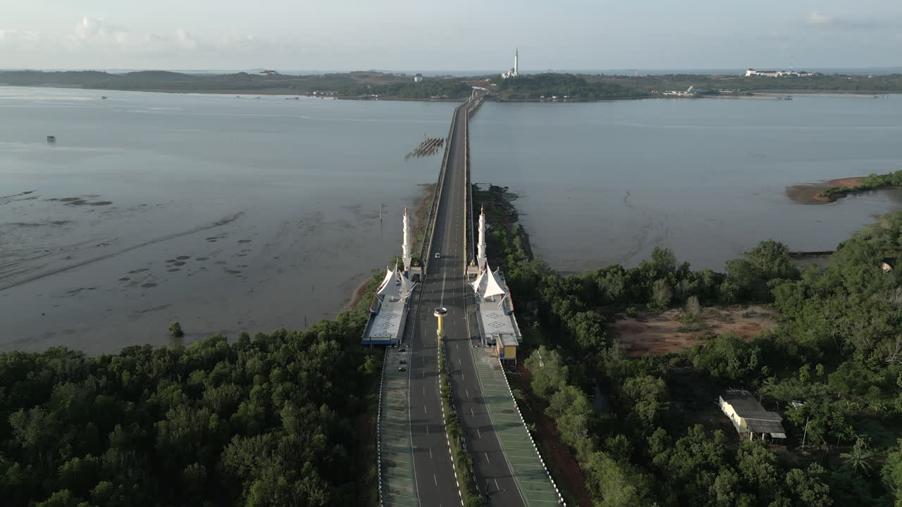 Cinematic drone tracking shot following the Jembatan Dompak as it leads to Masjid Raya Nur Ilahi at sunrise