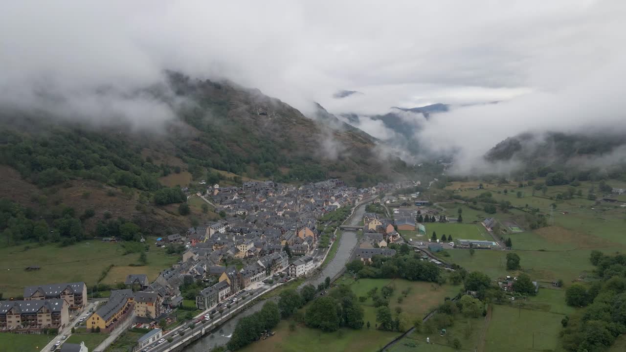 una impresionante toma de alta altitud captura un pequeño pueblo español anidado dentro de las majestuosas montañas de los pirineos, ofreciendo una impresionante vista panorámica