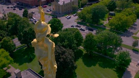 360 drone shot over the shoulder of the gold statue of lady justice on top of the beautiful courthouse in canandaigua, new york near canandaigua lake