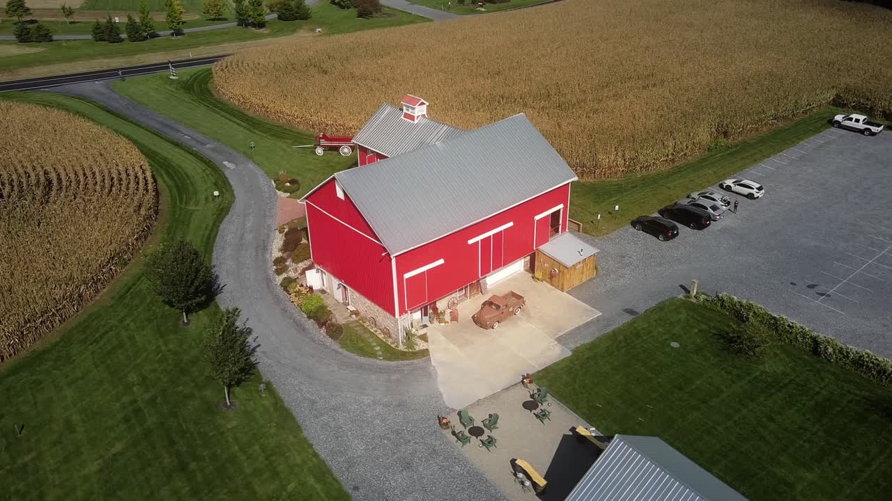 Aerial drone view of a red barn wedding venue with garden party concept, red house flanked by wheat fields and driveway seen from the road, wedding hall