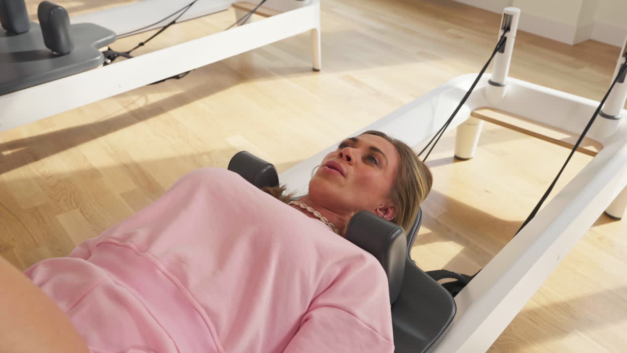 Ung kvinde liggende på ryggen på vognen af Pilates Reformer-udstyr. - nærbillede