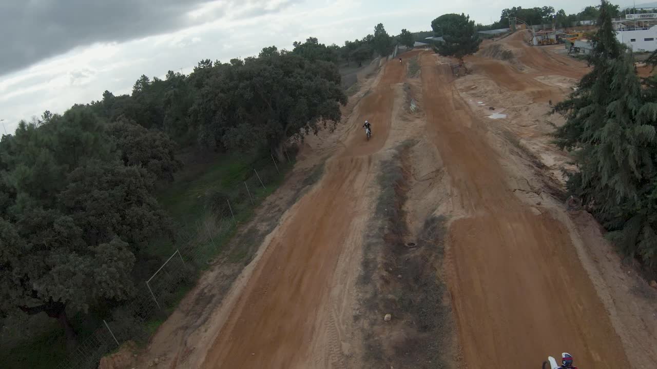 cámara lenta fpv aérea sincronizada con pilotos de motocross dando un salto de tierra en el día nuboso