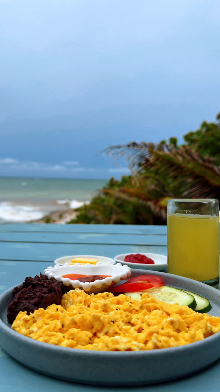 Colazione tropicale in riva all'oceano. Uova strapazzate, fagioli, verdure e succo serviti in un luogo tropicale sul mare