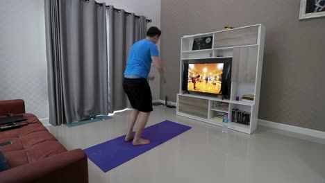 An-adult-man-is-doing-push-ups-and-jumping-in-front-of-a-television-in-his-living-room-following-a-fitness-programme-moves