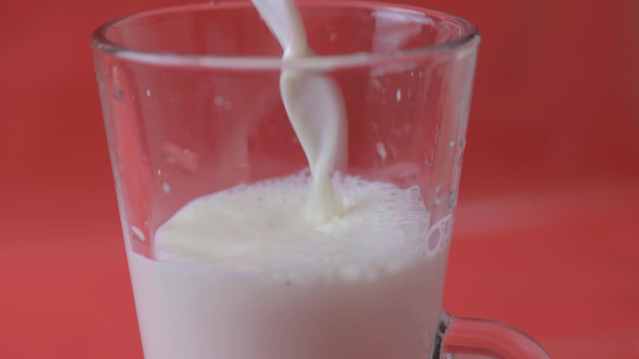 verter leche en un vaso sobre un fondo rojo.